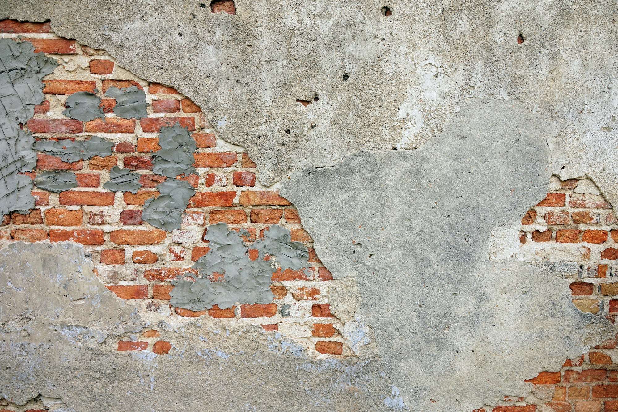 Mur de briques rouges partiellement recouvert d’enduit gris