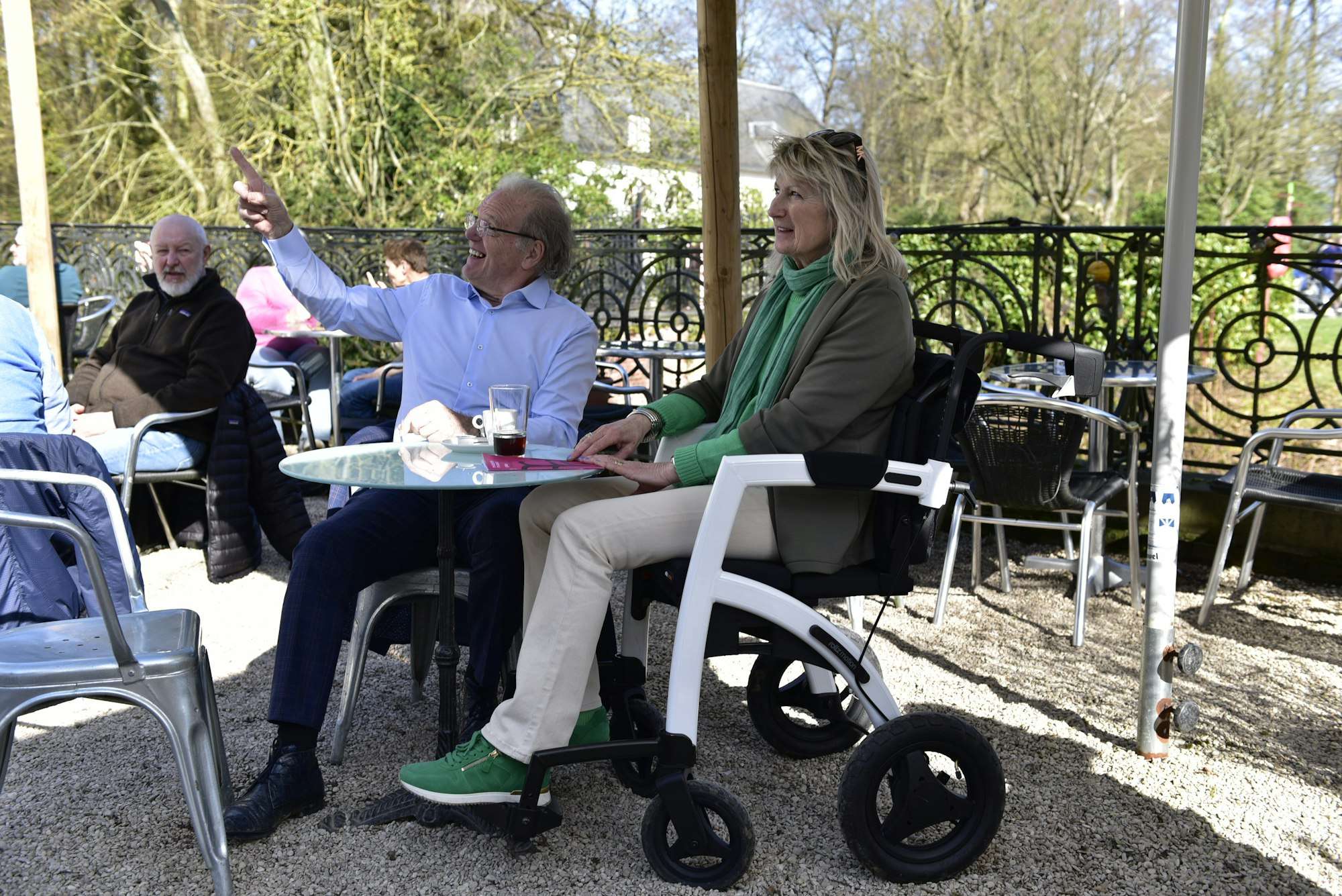 Des personnes âgées discutent à une terrasse ; l’une d’elles est assise en fauteuil roulant