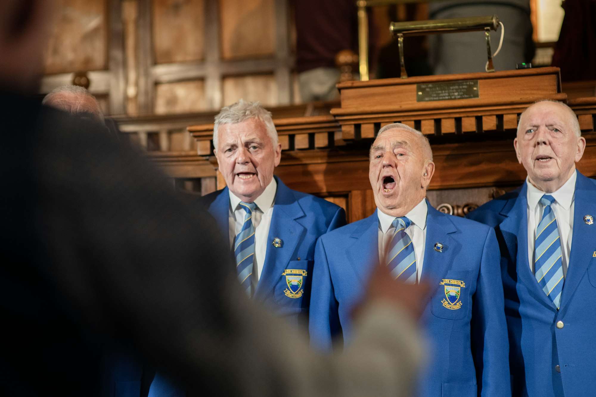 Trois hommes âgés en blazer bleu chantent à pleine voix