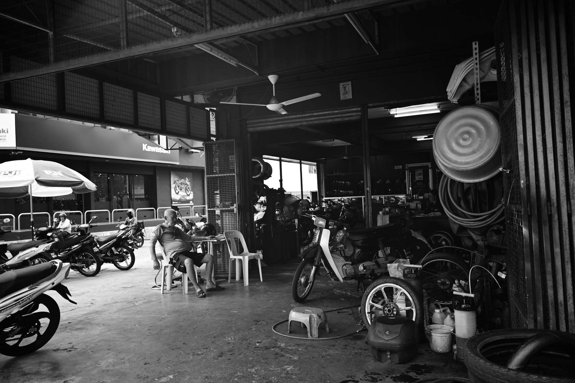 Motos alignées sous la charpente d’un atelier, en noir et blanc