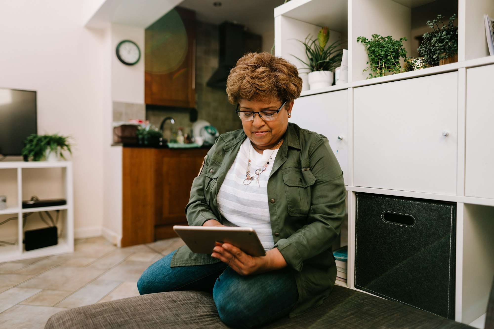 Une femme consulte une tablette, assise chez elle