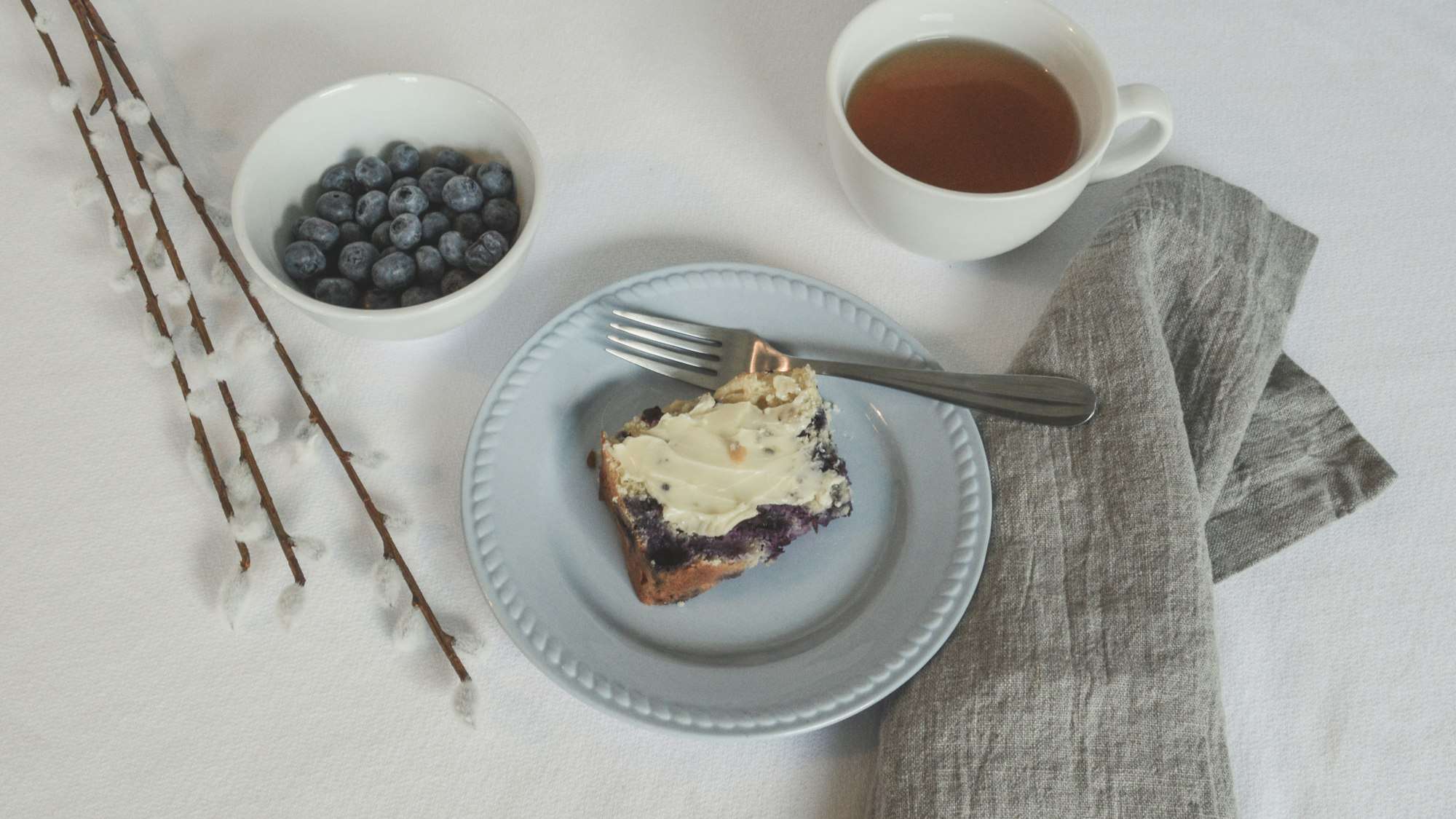Petit-déjeuner sur une table claire : thé, myrtilles, tartine et serviette de lin