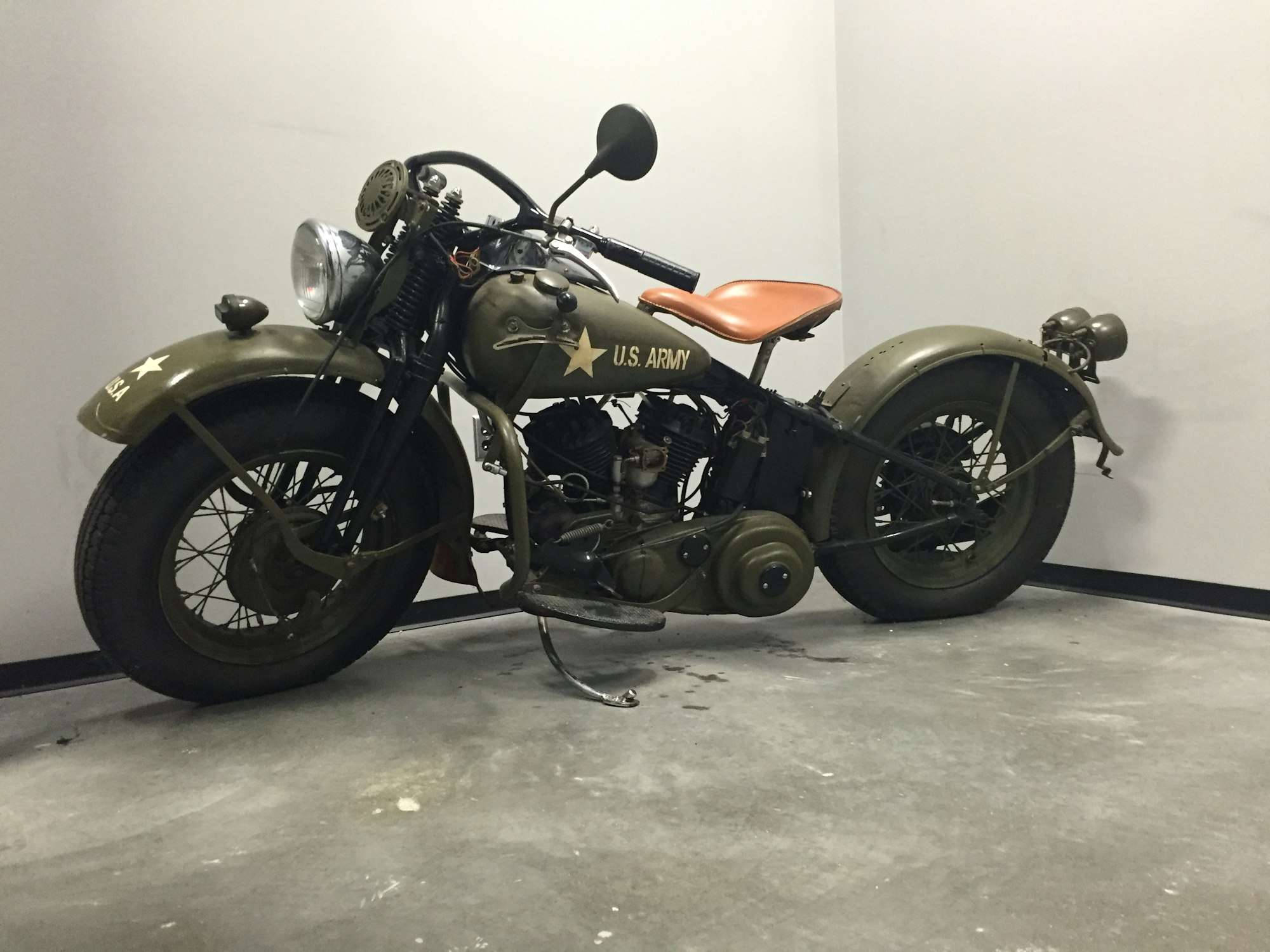 Moto militaire ancienne vert olive, selle en cuir, dans un atelier blanc